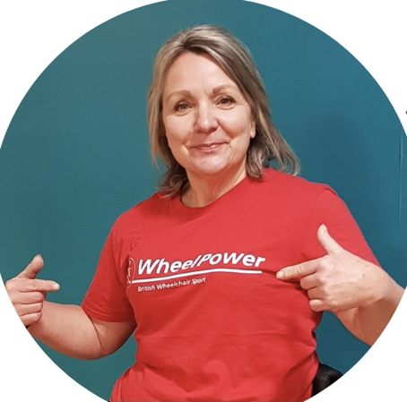 A photograph of a woman wearing a red tshirt. She is pointing to the words "Wheelpower" on the tshirt.
